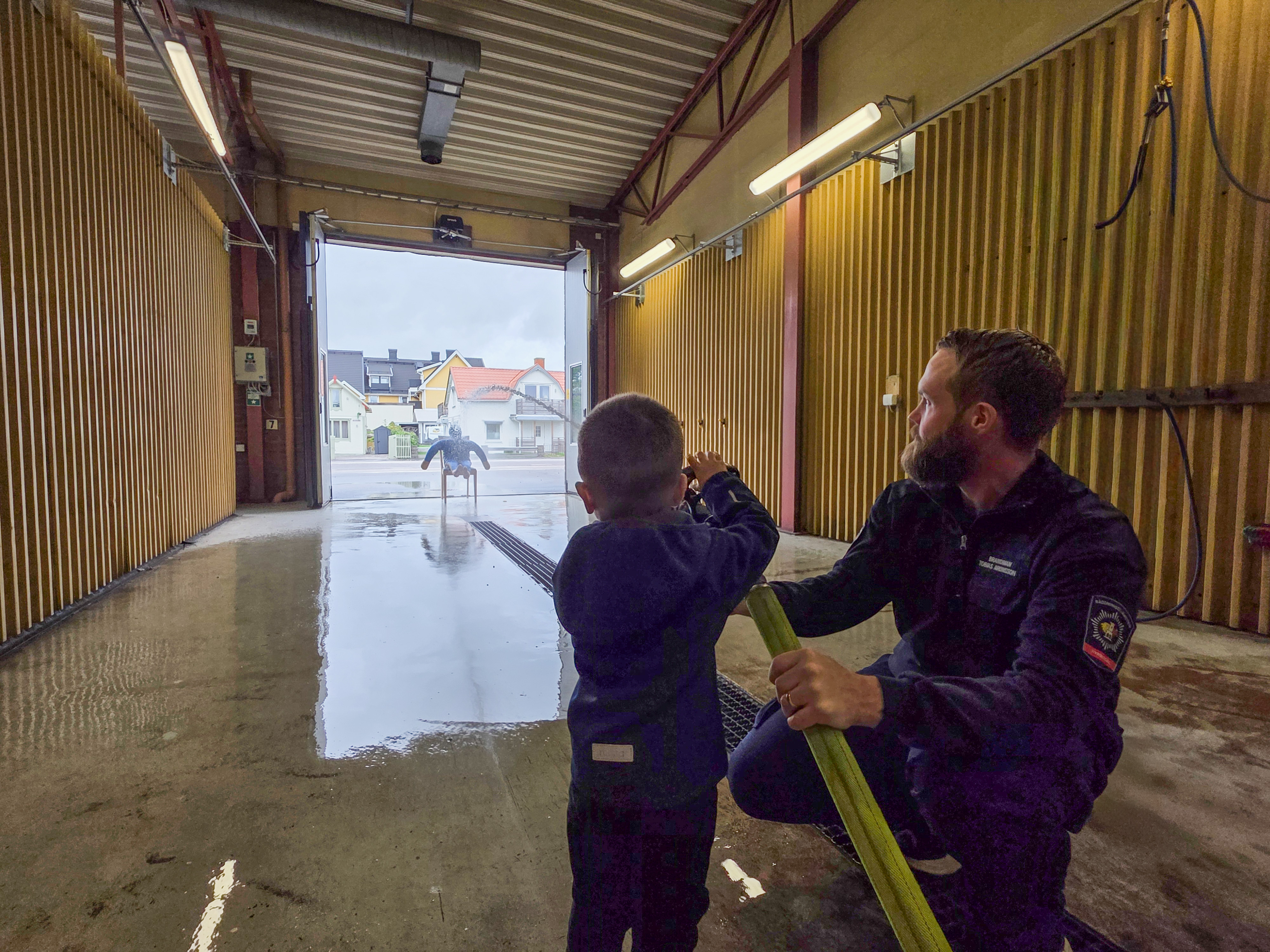 Barn testar brandslang tillsammans med brandman.