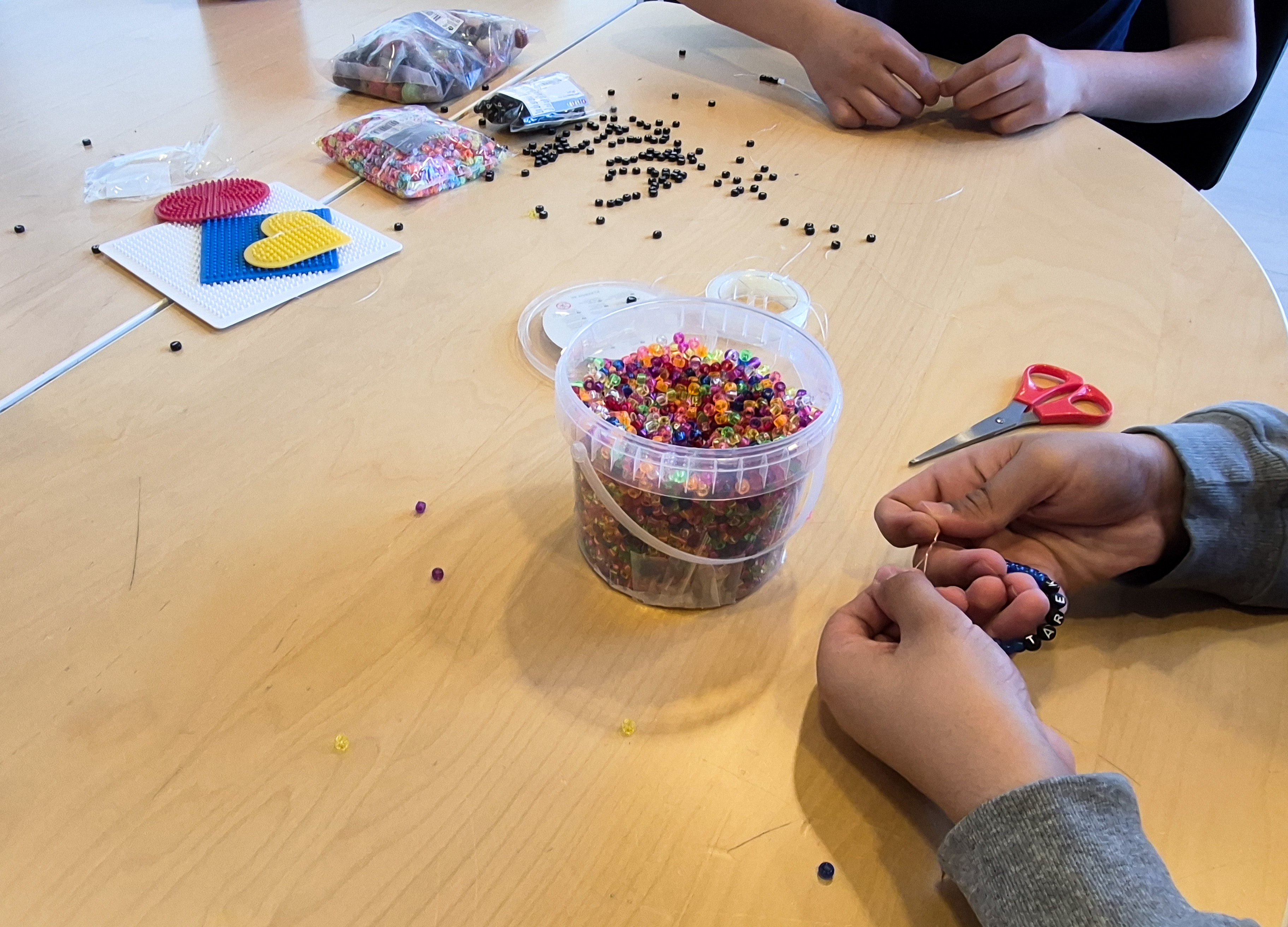 Närbild på händer och pärlor. Händerna håller på att knyta en knut på ett armband som de precis har gjort.