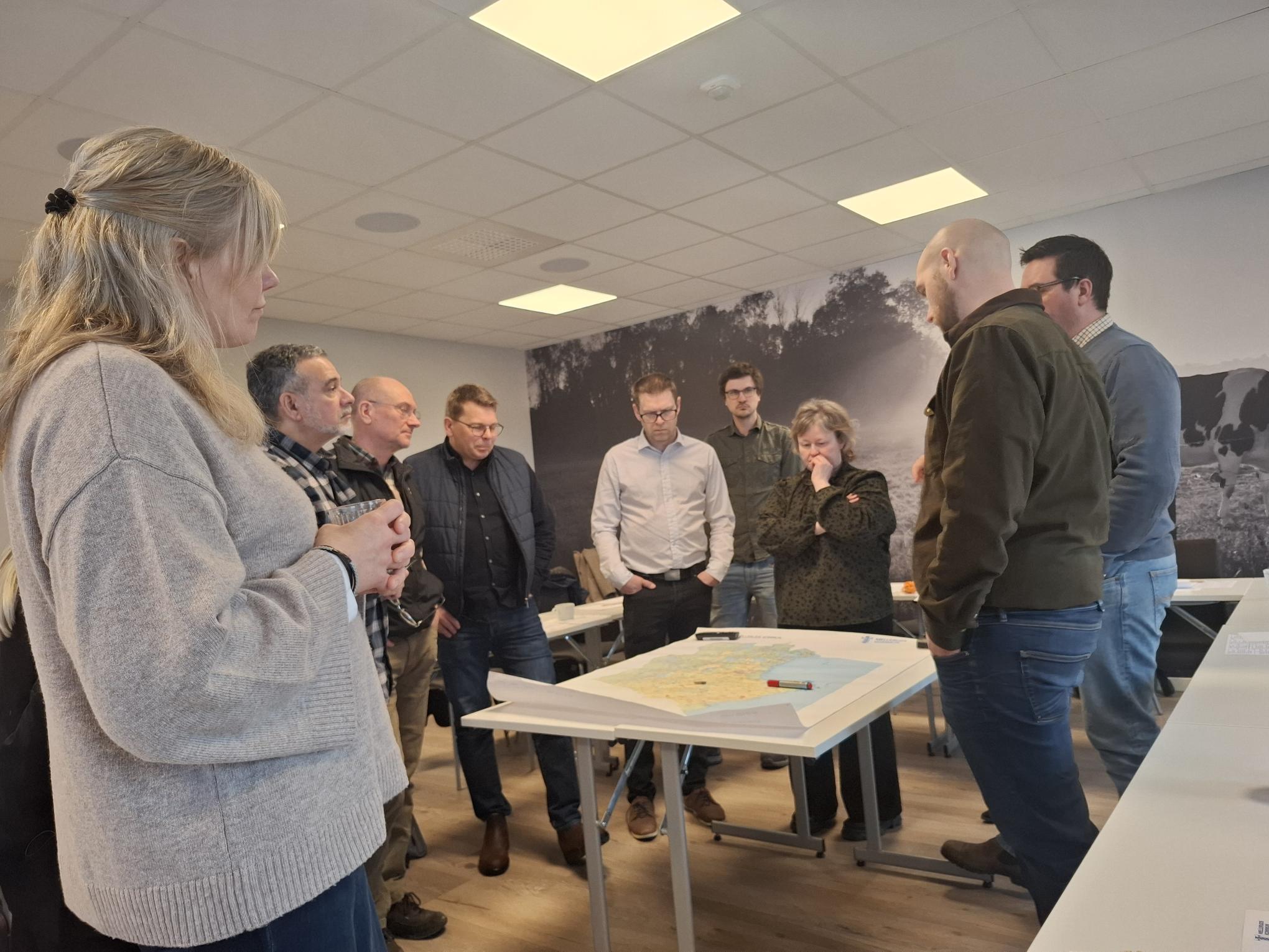 Personer står runt ett bord med en karta