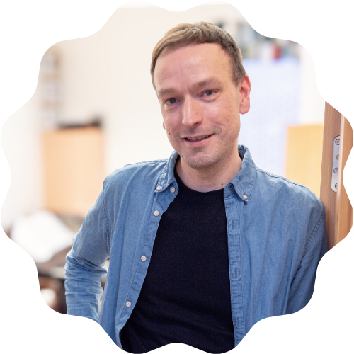 Foto på glad Tommy i blå jeansskjorta lutandes mot dörrkarmen.