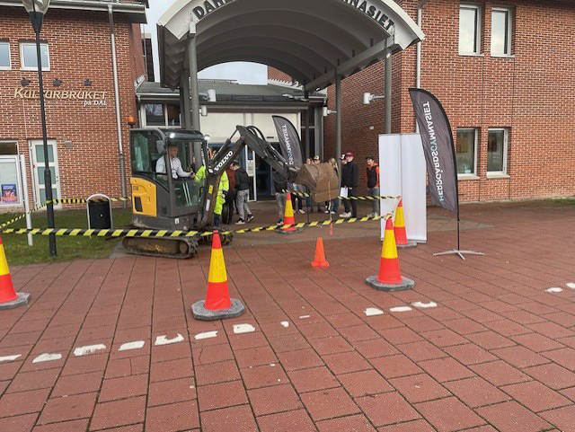 Elever utanför Rådaskolan, varav en provsitter i en liten grävmaskin innanför en liten avspärrning