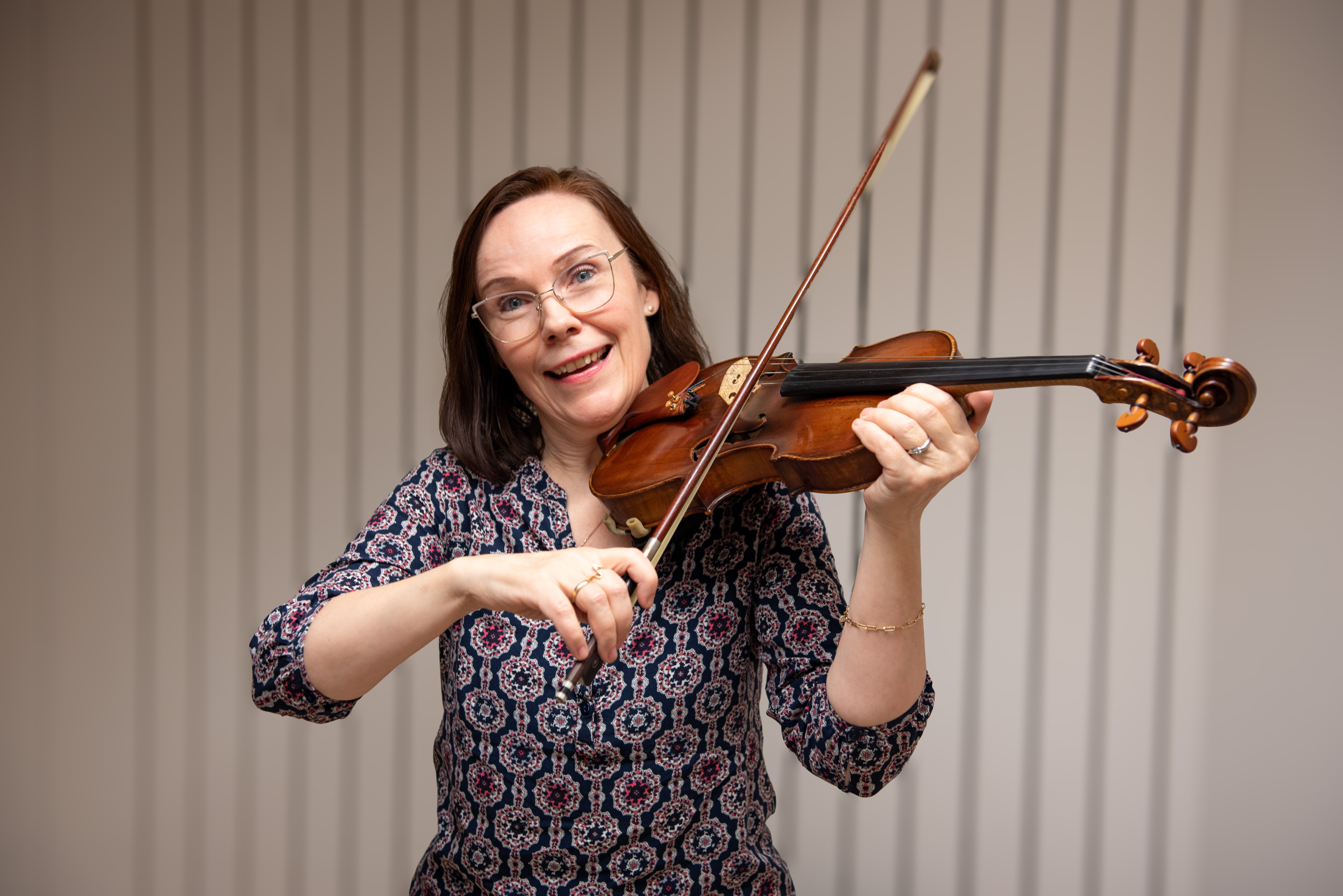 Bild på en glad stråklärare mot en vit akustikpanel hållandes i en fiol.