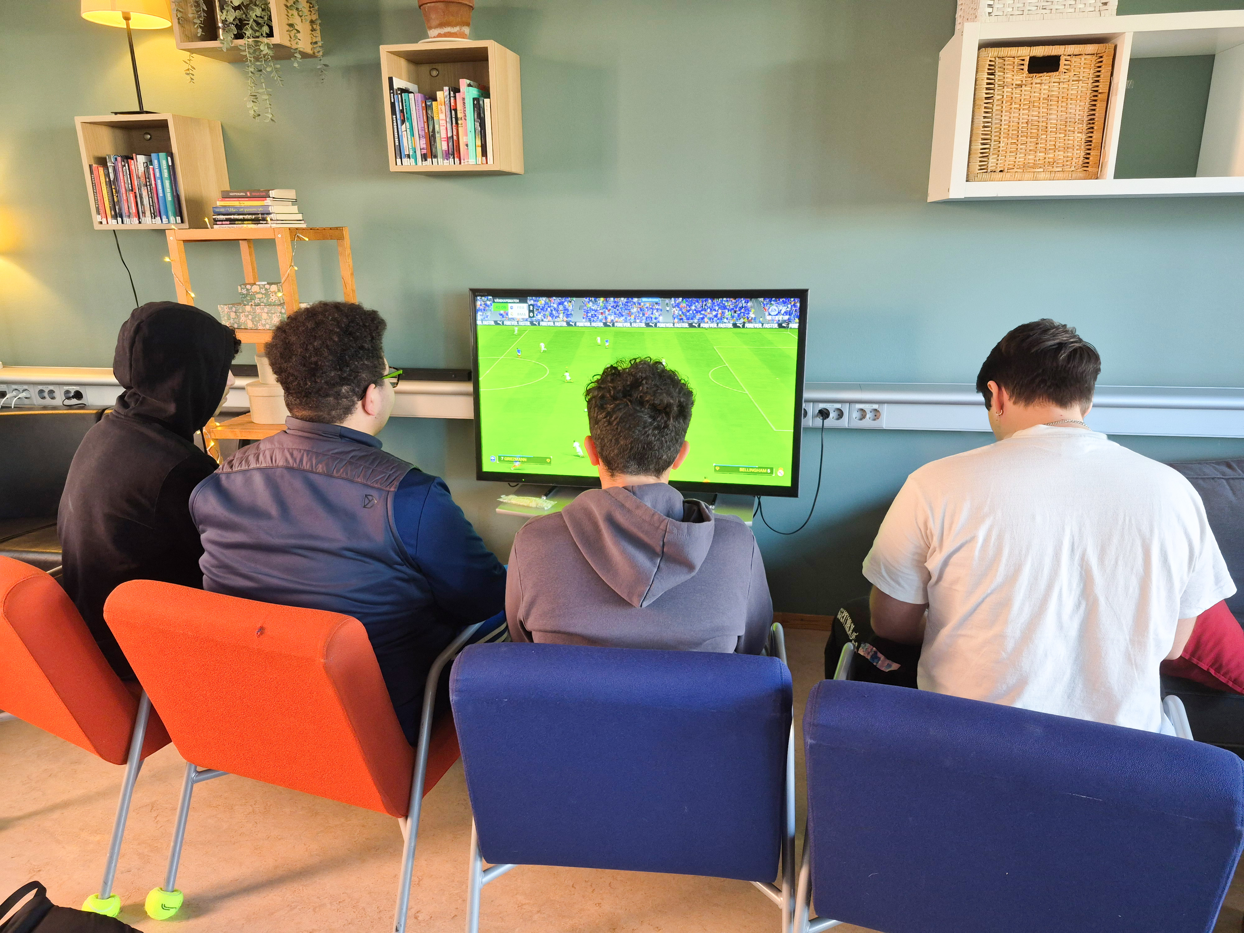 fyra ungdomar sitter och spelar tv spel där de spelar fotboll