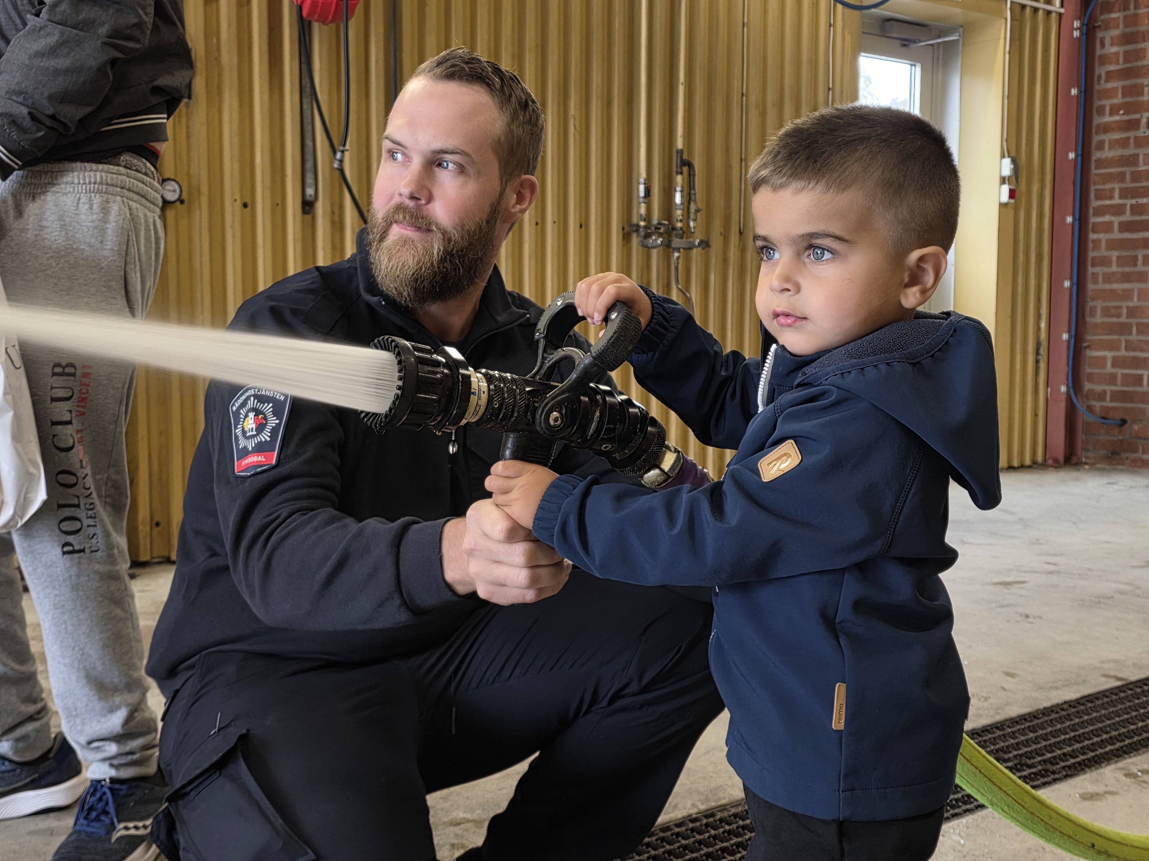 Barn testar brandslang tillsammans med brandman.