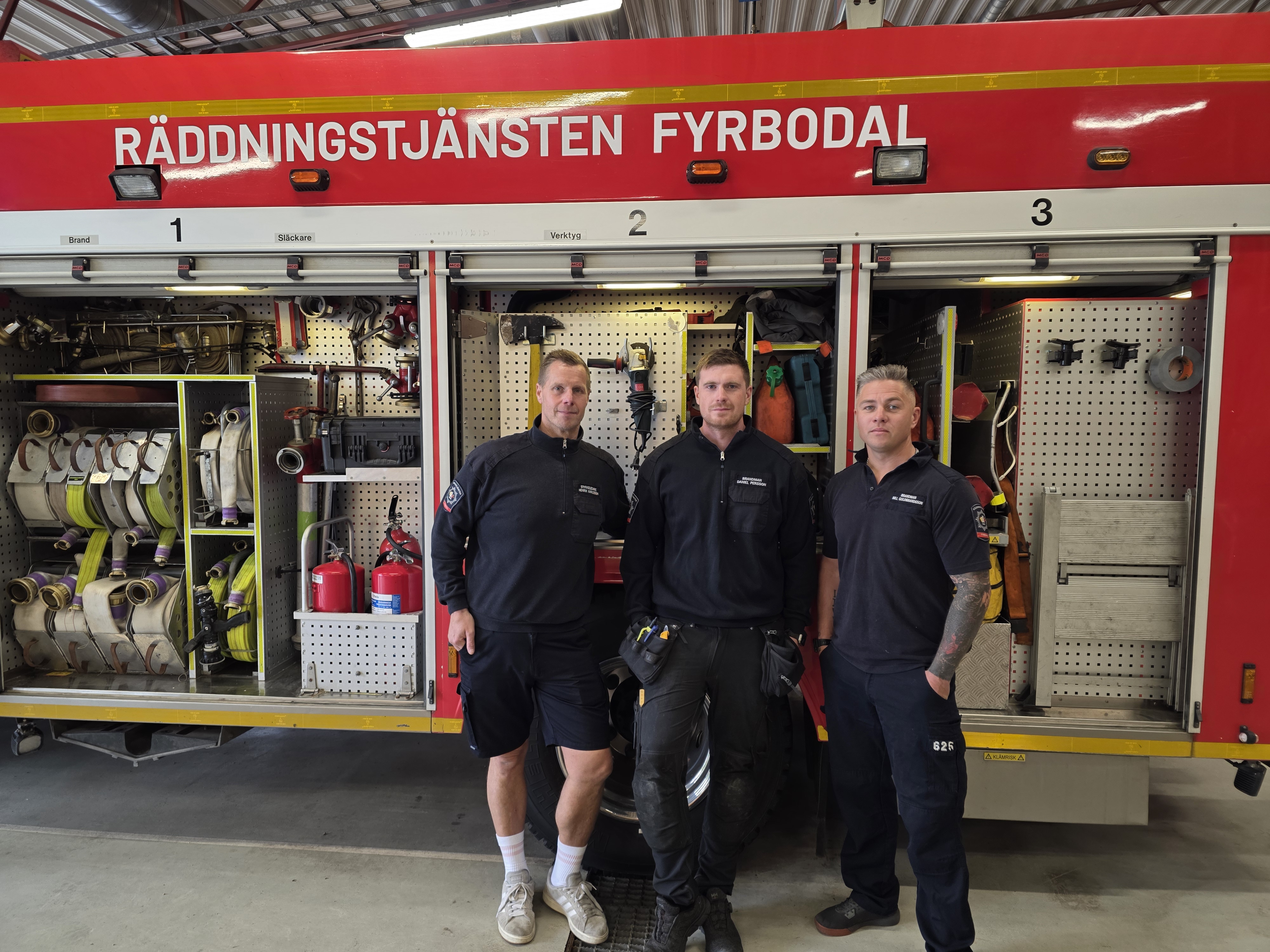 Tre brandmän framför en brandbil