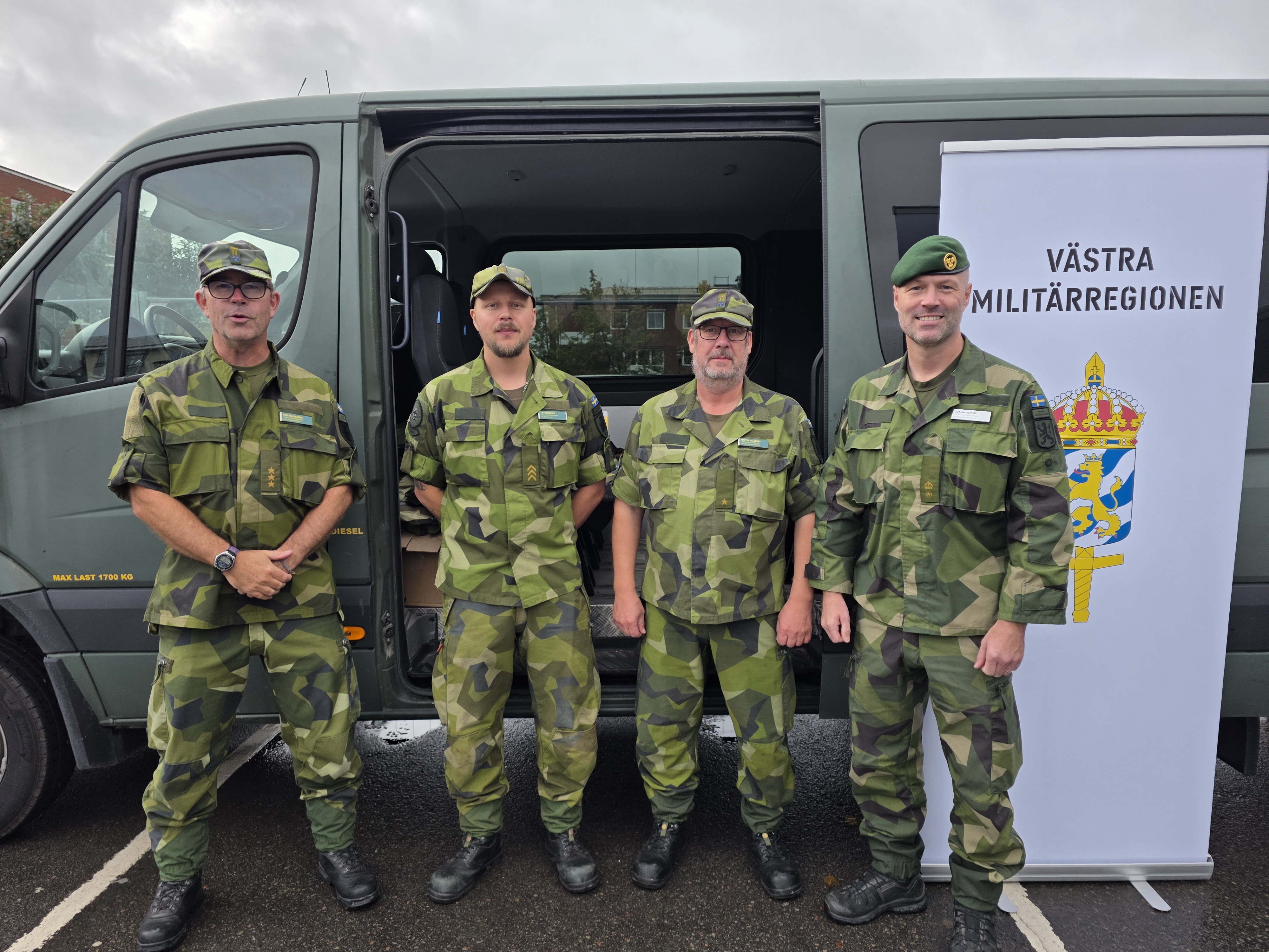 Tre militärer står uppställda framför en grön bil.