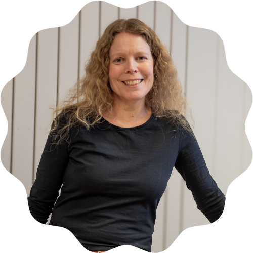 Foto på en leende lärare Elin mot en vit akustikvägg i sitt klassrum.