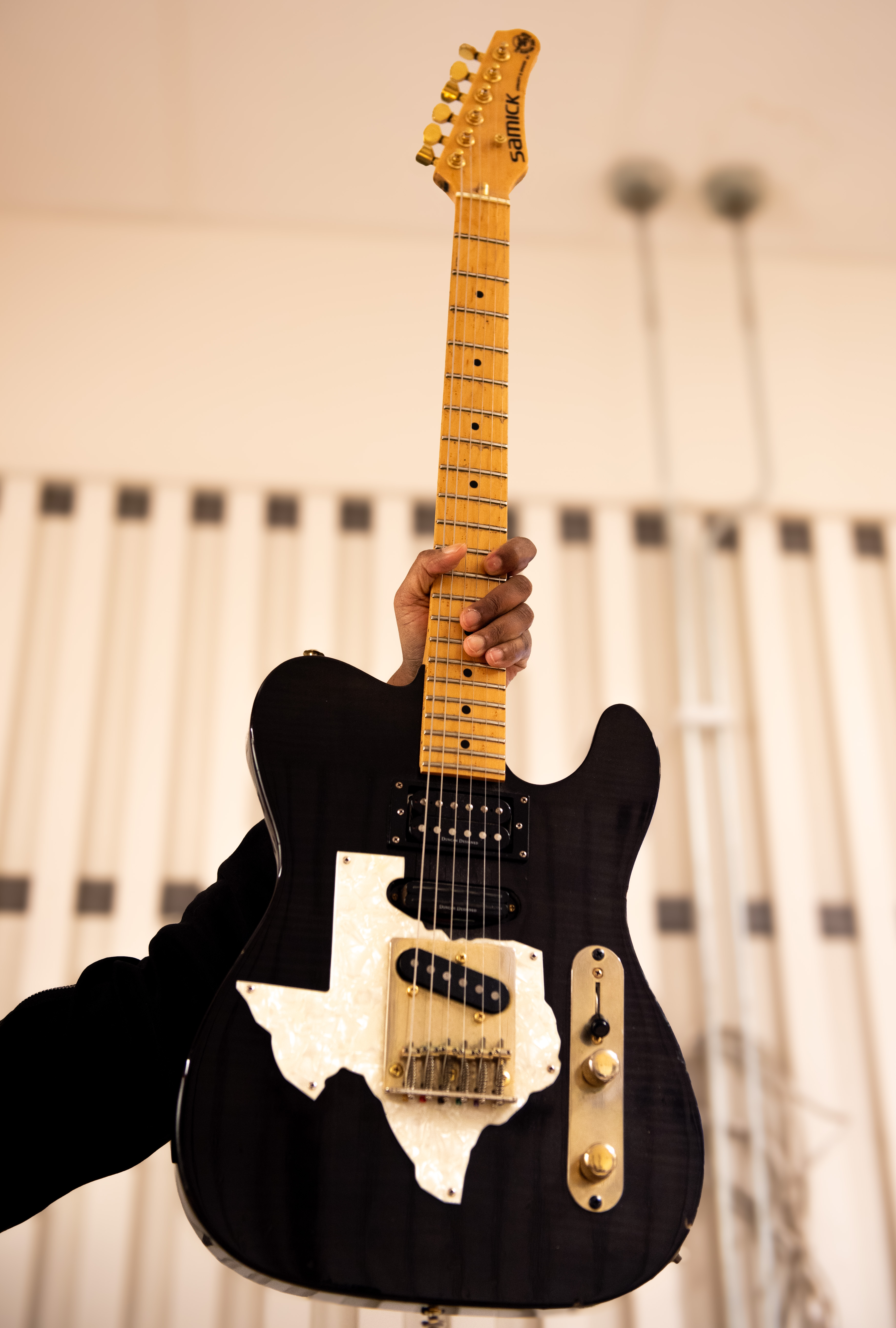 Bild på en svart elgitarr mot en vit akustikpanel