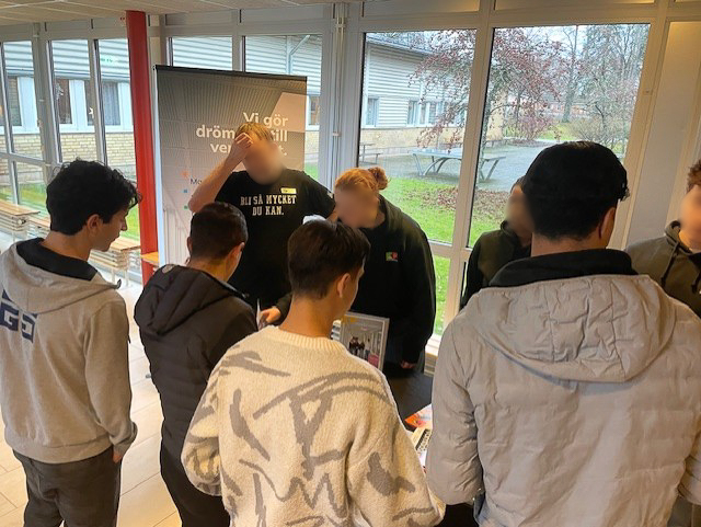 Elever tittar intresserat vid ett bord där representanter från en gymnasieskola står
