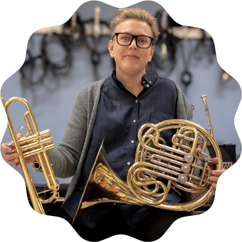 Foto på lärare Cici som sitter hållandes i ett valthorn och trumpet