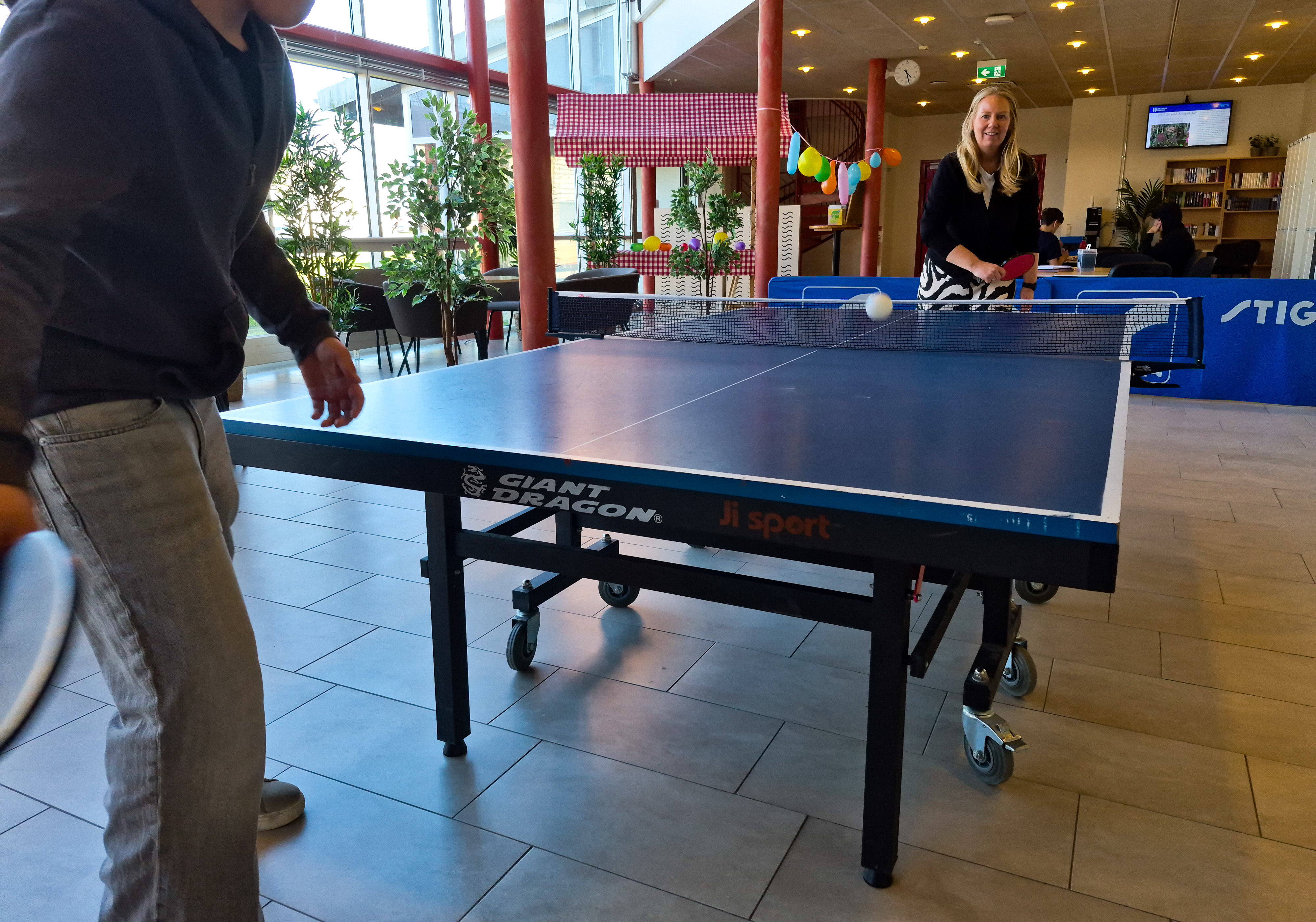 en ungdom spelar pingis mot en i personalen och bollen studsar på bordet