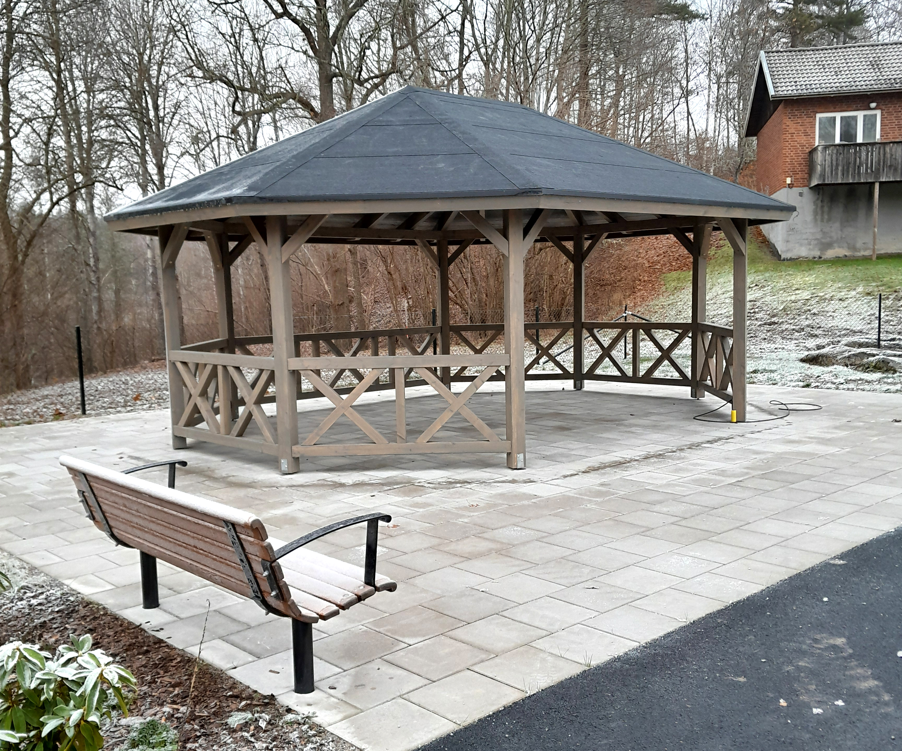 En stor och rymlig Paviljong, med en bänk framför och marken är belagd med stenplattor